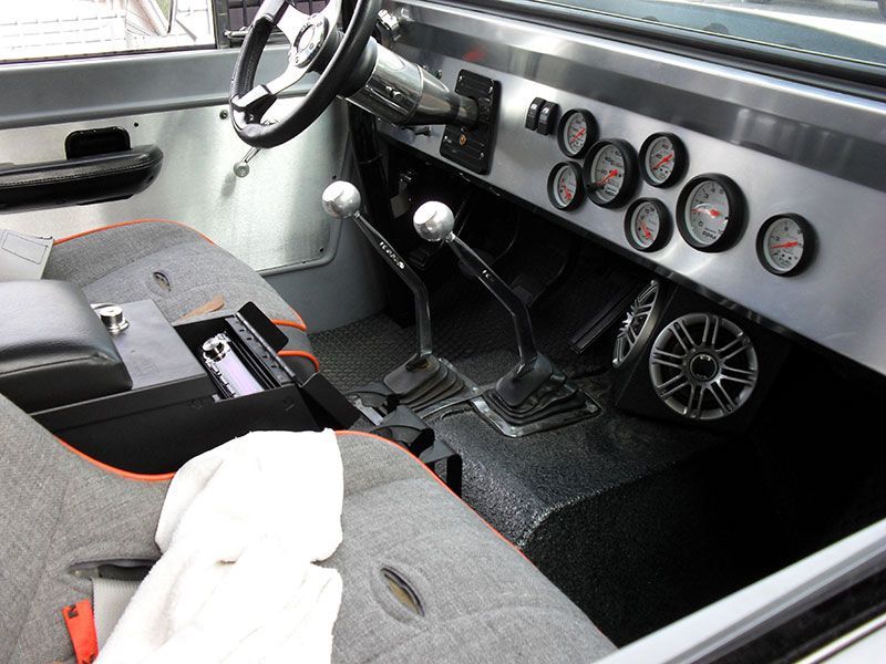 Vintage car interior with black-and-white seats, steering wheel, manual shifter, and dashboard gauges