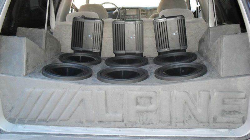 Car trunk with three black speakers and subwoofer openings built into a custom Alpine panel