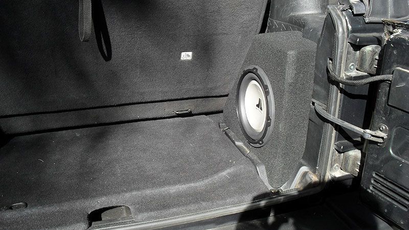 Black vehicle trunk interior with a round speaker and folded seat panel.