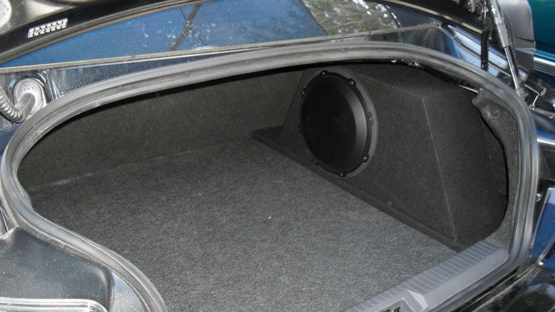 Car trunk interior with gray carpet and a circular speaker enclosure on the right side