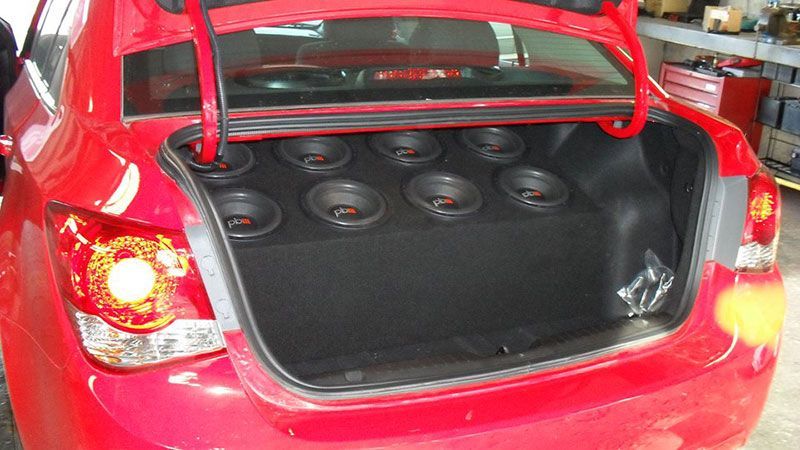 Red car trunk open with several subwoofer speakers installed in the cargo area
