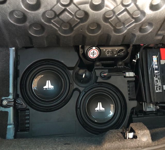 Car trunk with two black JL Audio subwoofers and an amplifier installed in a custom enclosure.