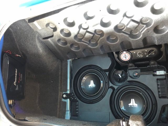 Car audio subwoofer enclosure with two JL Audio speakers under a textured trunk lid