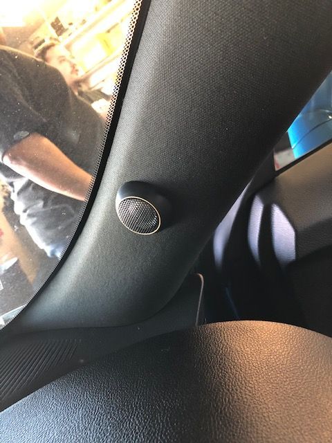 Close-up of a car door speaker and interior trim, with a person standing outside in the background.