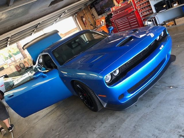 Blue sports car in a garage, driver door open, front view with black accents