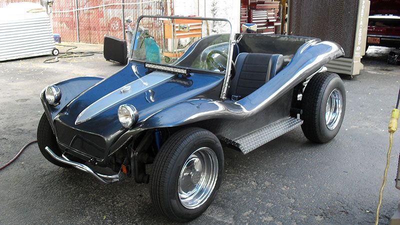 Black dune buggy with blue stripe parked indoors on a concrete floor