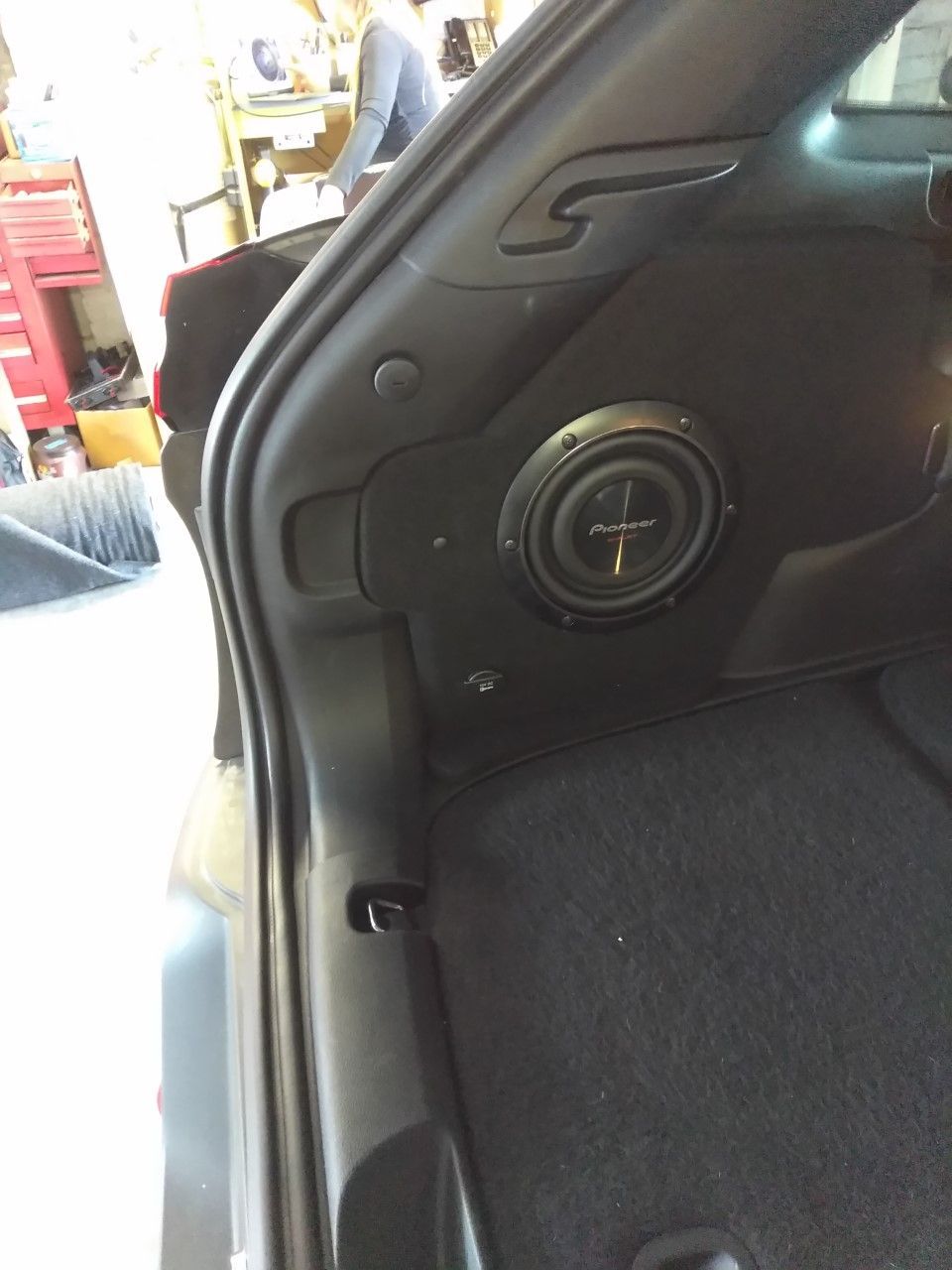 Close-up of a car’s interior side panel with a round speaker grille and black upholstery.
