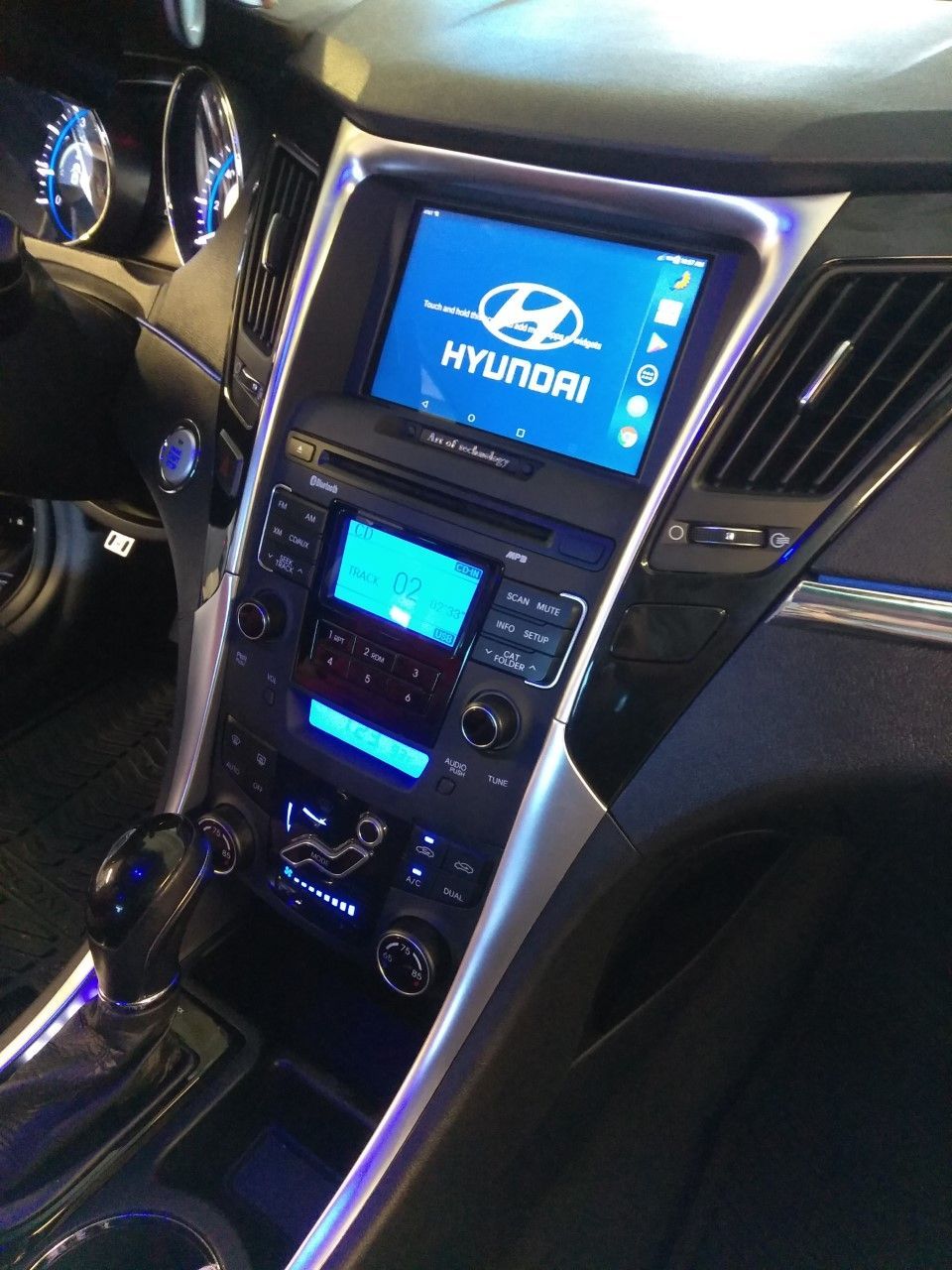 Car dashboard with Hyundai infotainment screen and center console lit in blue at night