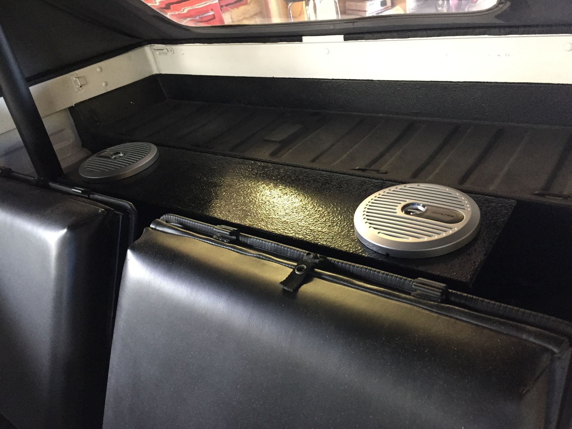 Two round speakers mounted on a black ledge above a vinyl seat inside a vehicle cabin