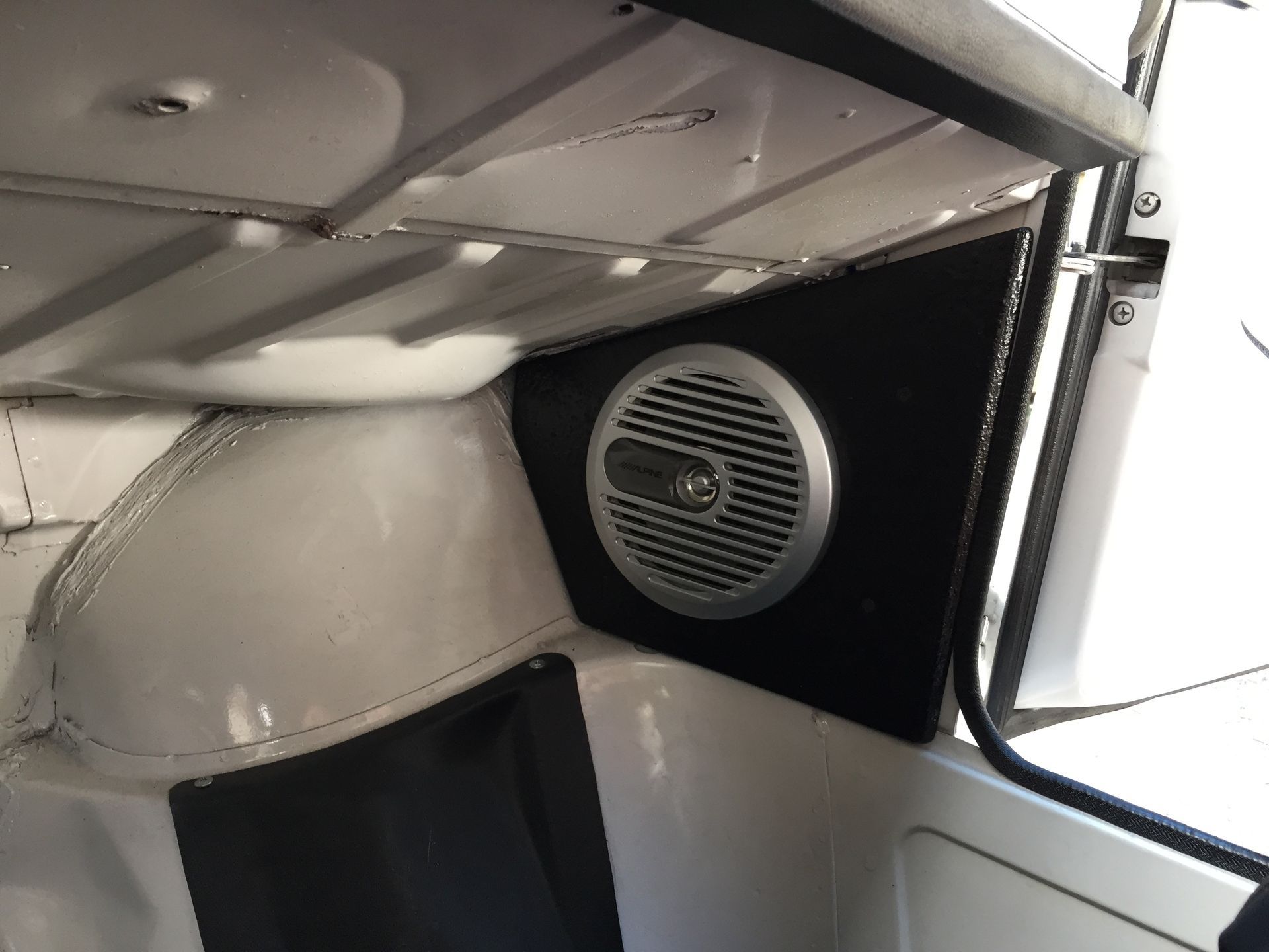Interior of a vehicle with a round speaker mounted beside a window and silver ceiling panels