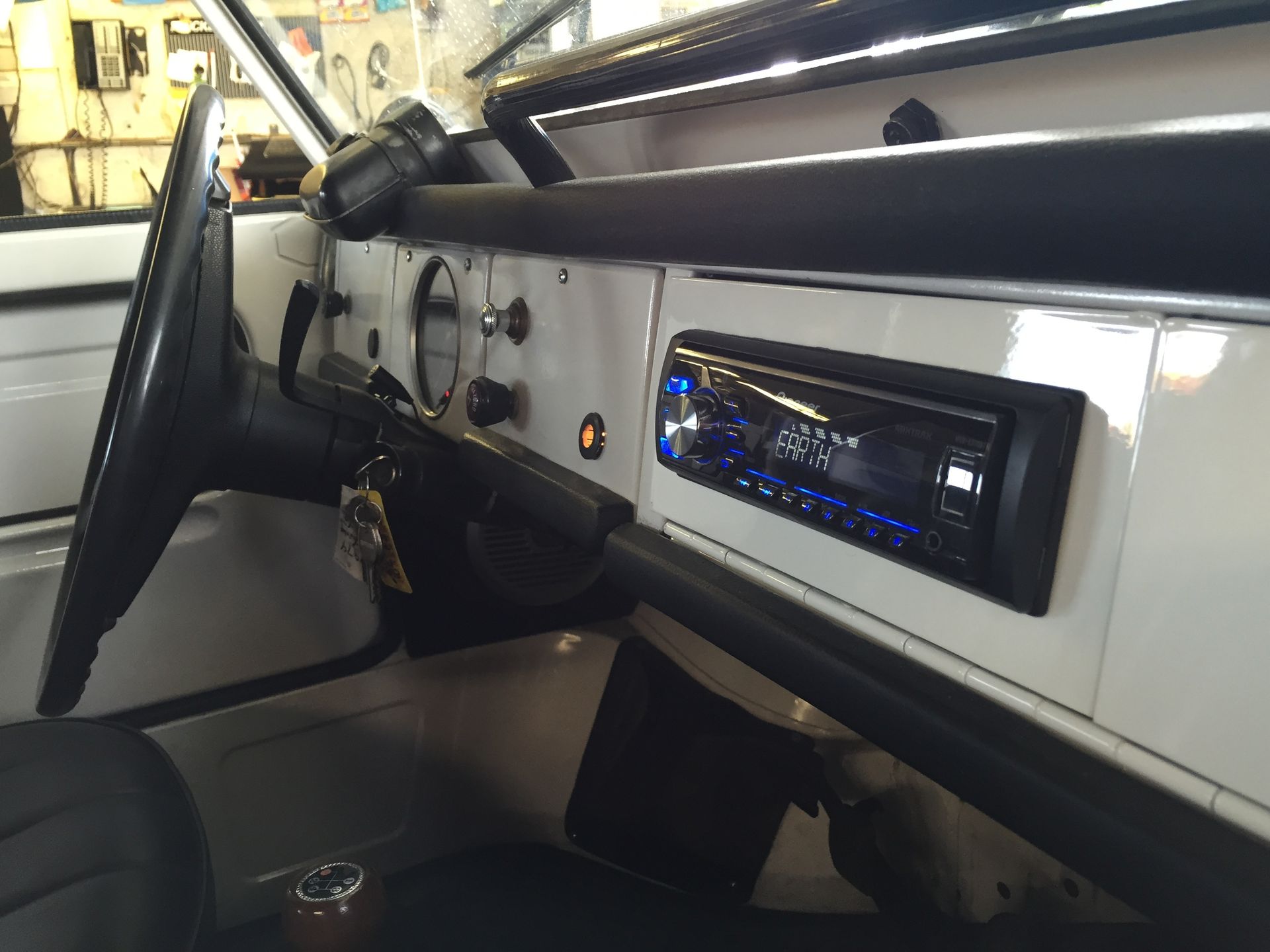 Classic car interior with open door, white dashboard, and blue-lit stereo.