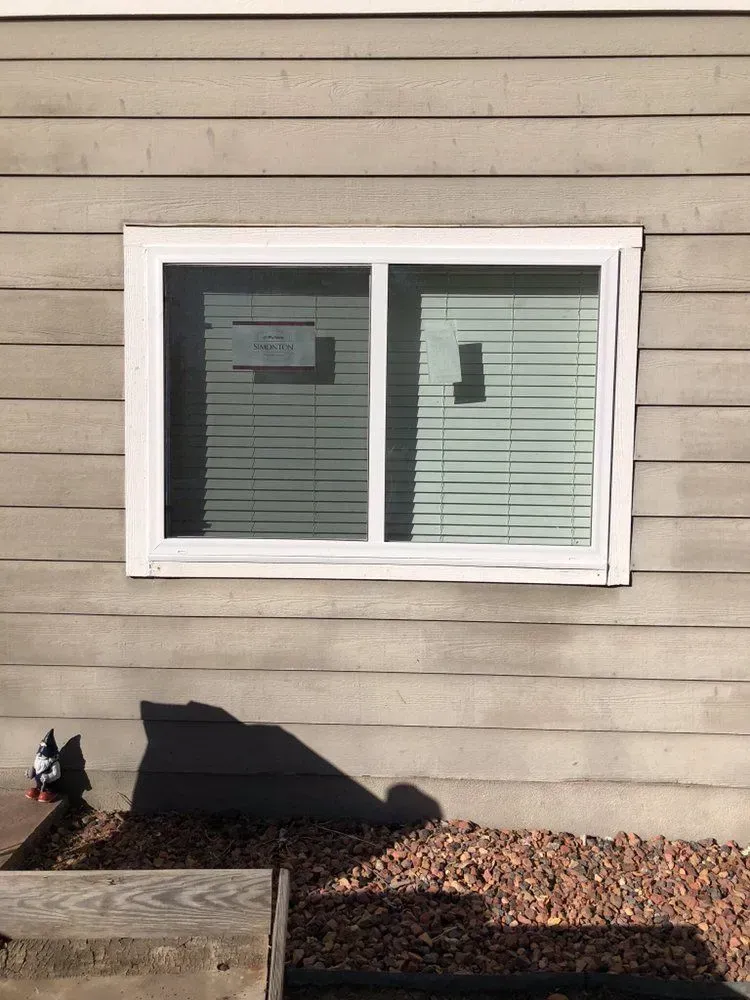 White-framed window on beige siding above a small stone-bordered garden bed.