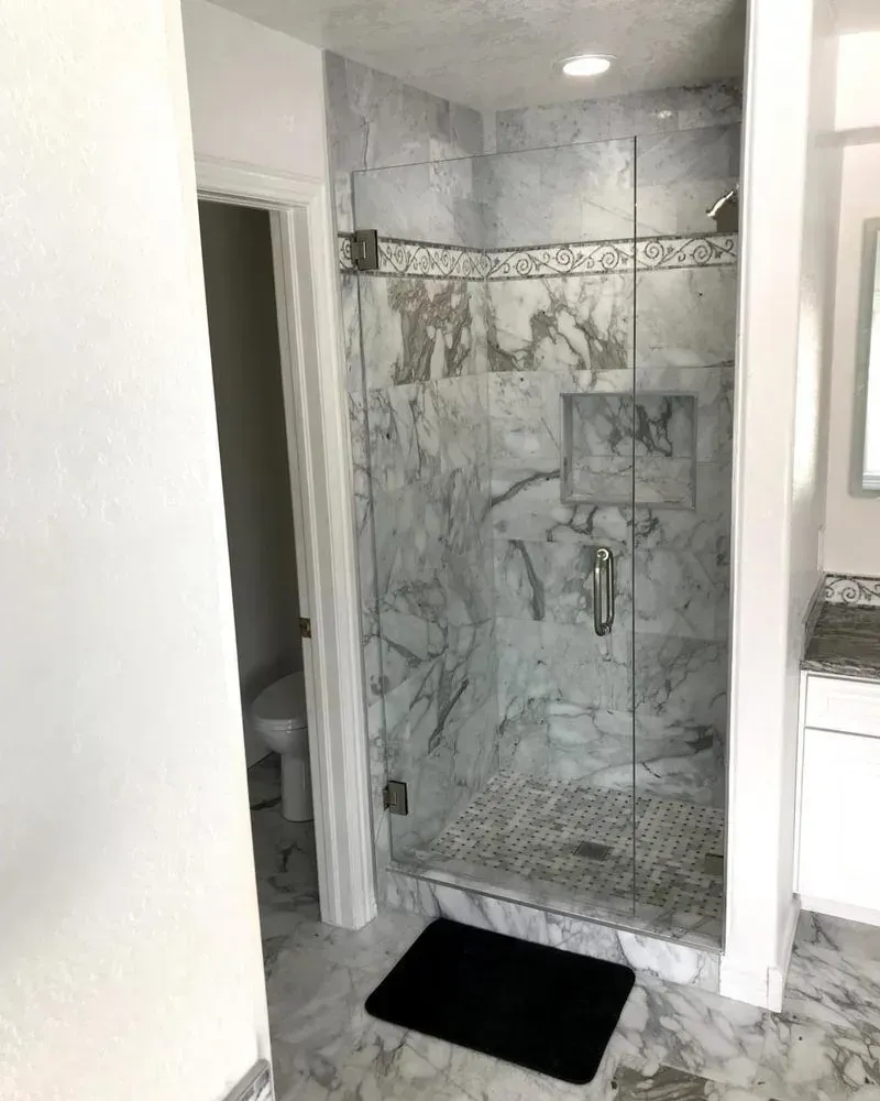 Marble-tiled bathroom shower with glass enclosure and black bath mat