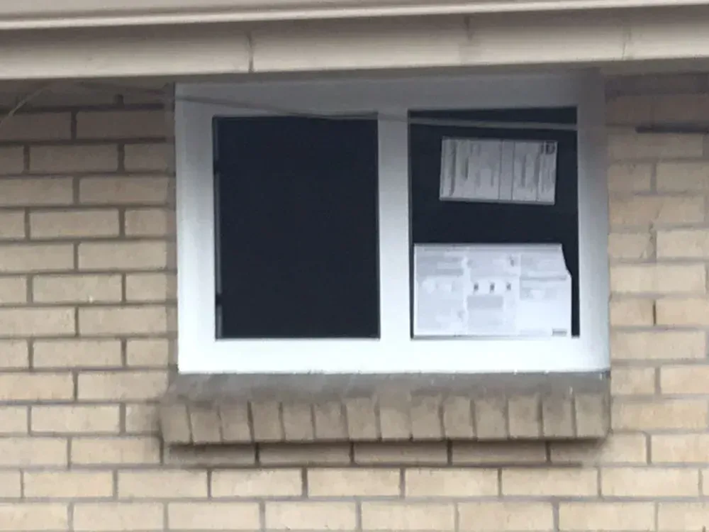 Brick building window with white frame, dark panes, and papers posted inside
