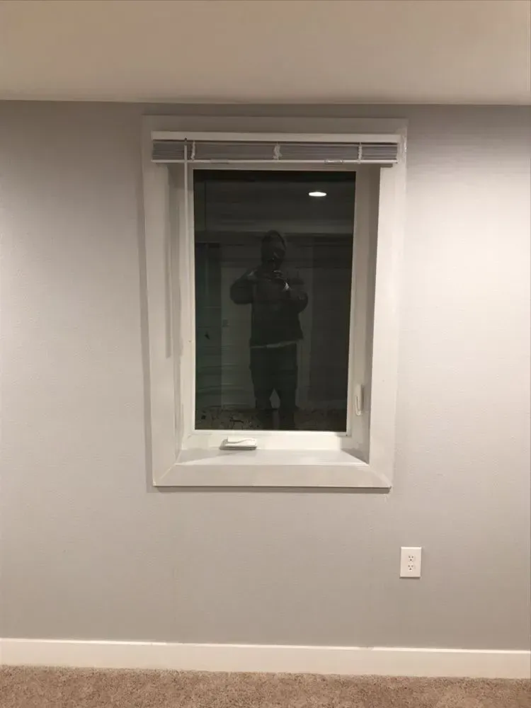 White wall with a small window; faint reflection of a person holding a camera.