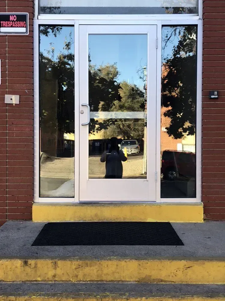 Glass double doors at a brick building entrance, with a black doormat and yellow curb step.