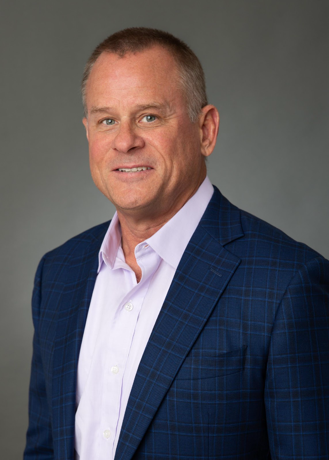 A man in a blue suit and pink shirt is smiling for the camera.