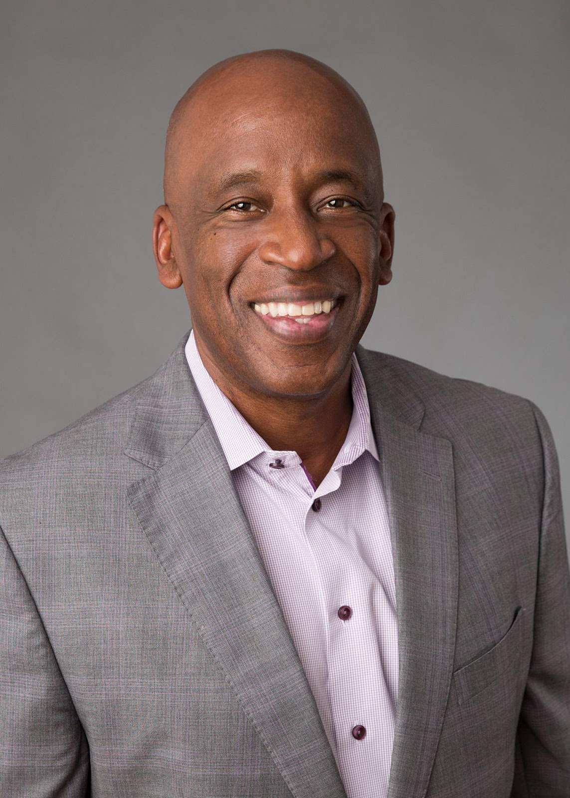 A man in a suit and purple shirt is smiling for the camera.