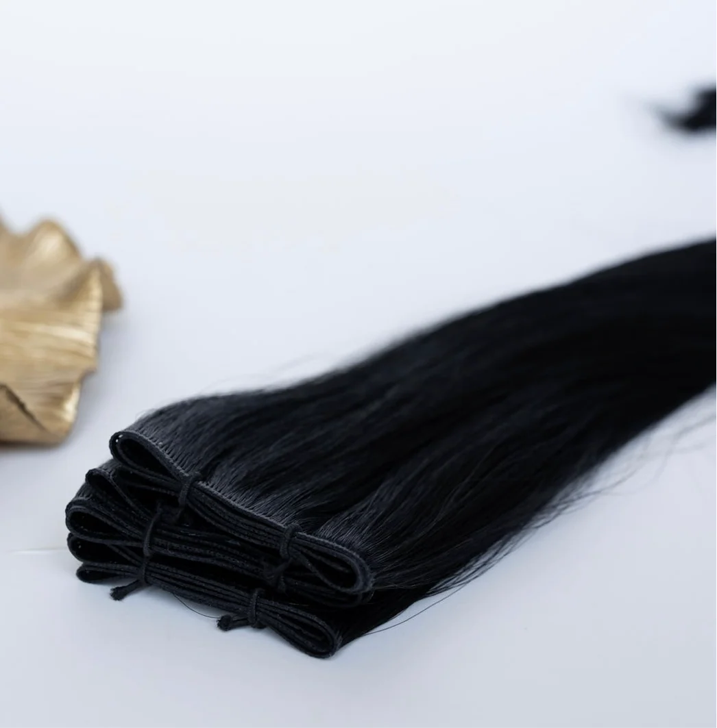 Black hair extensions laid out on a white surface, with a gold clip nearby