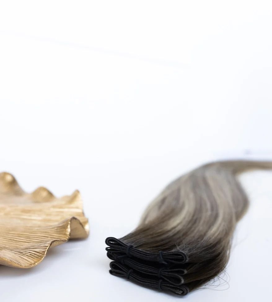 Black hair extension next to a gold seashell-shaped accessory on a white background
