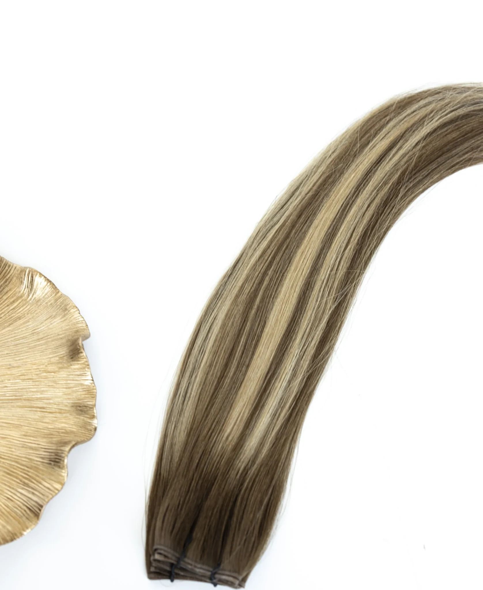 Close-up of beige braided hair extension next to a beige seashell on a white background