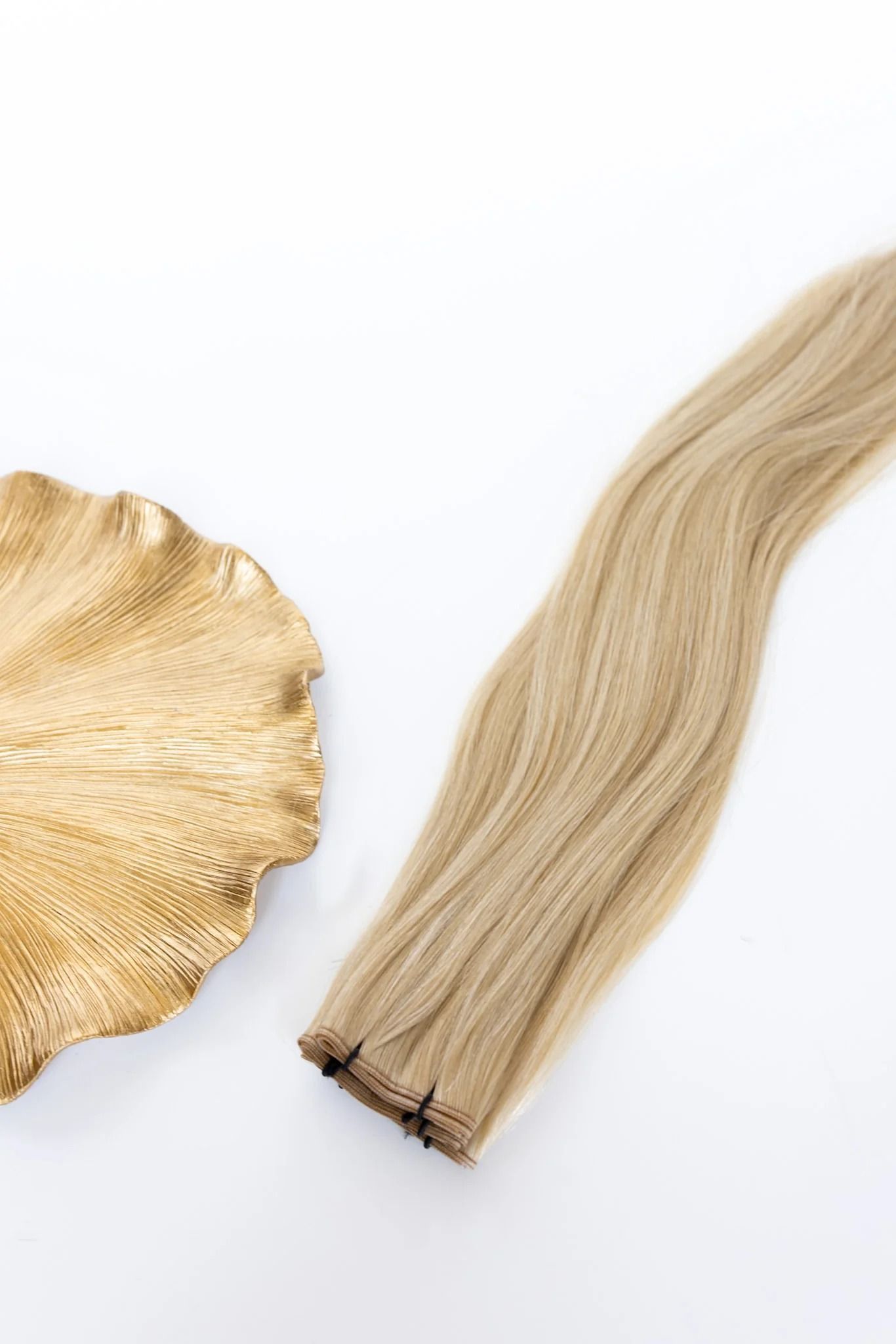 Blonde braided hair extension beside a gold, leaf-shaped decorative piece on a white background