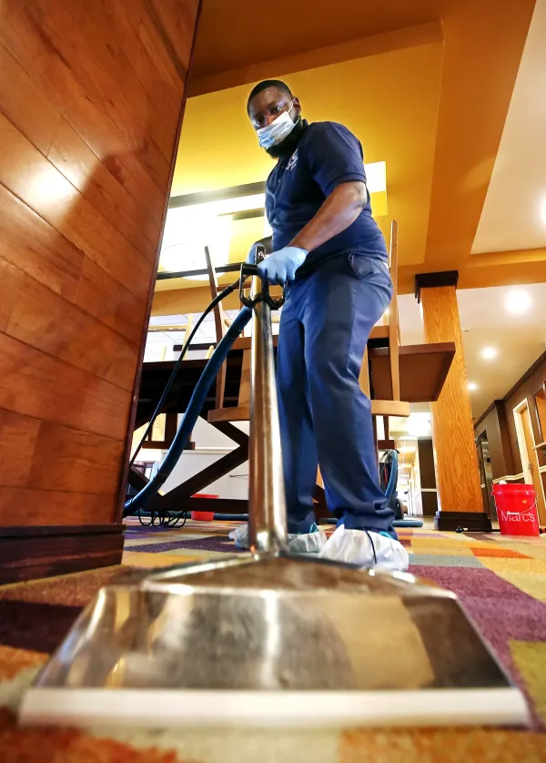 Person holding cleaning supplies, another mopping floor, in a well-lit room. Person holding cleaning supplies, another mopping floor, in a well-lit room.