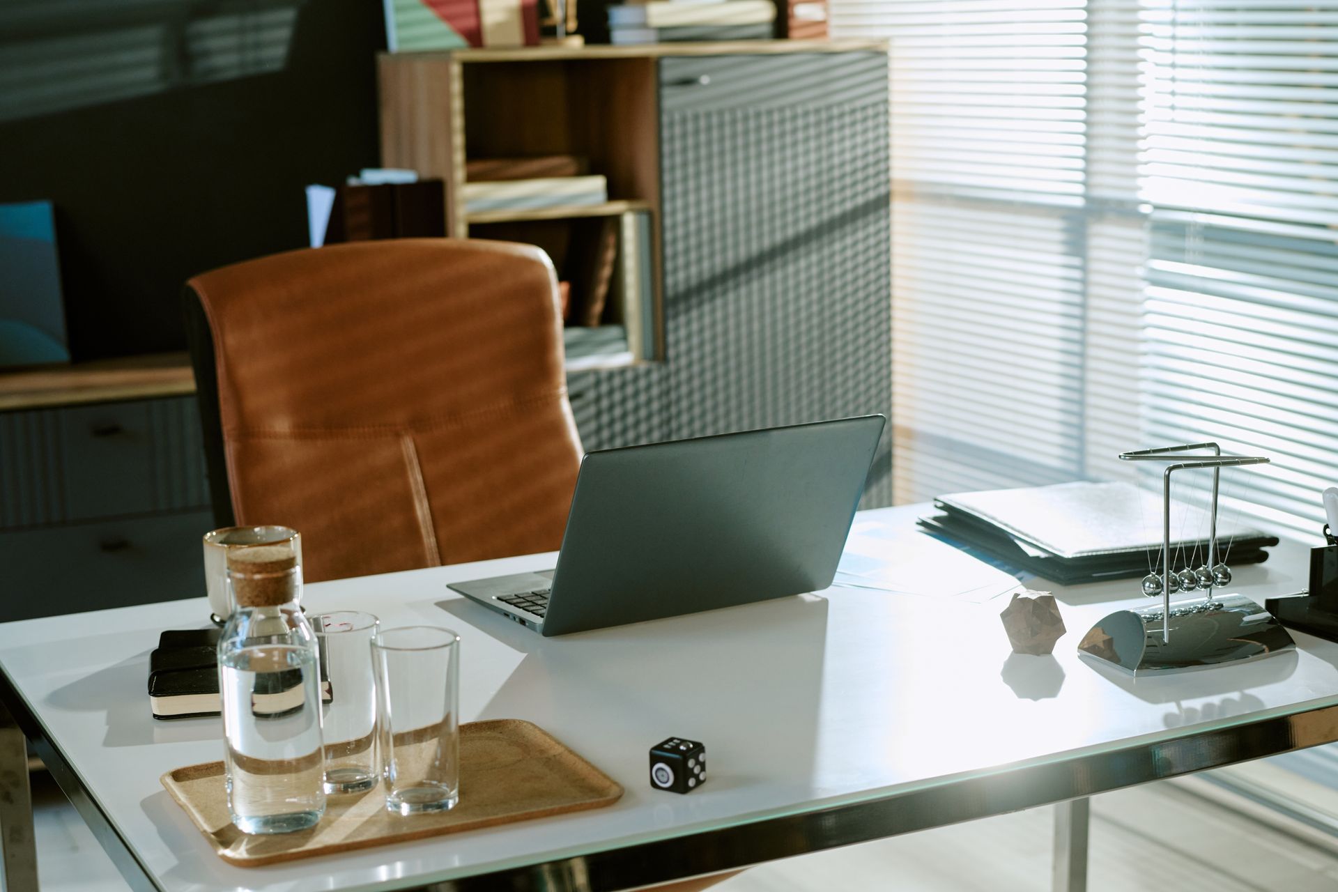 Modern office desk with open laptop, water bottle, glasses, chair, asnd window blinds Modern office desk with open laptop, water bottle, glasses, chair, asnd window blinds