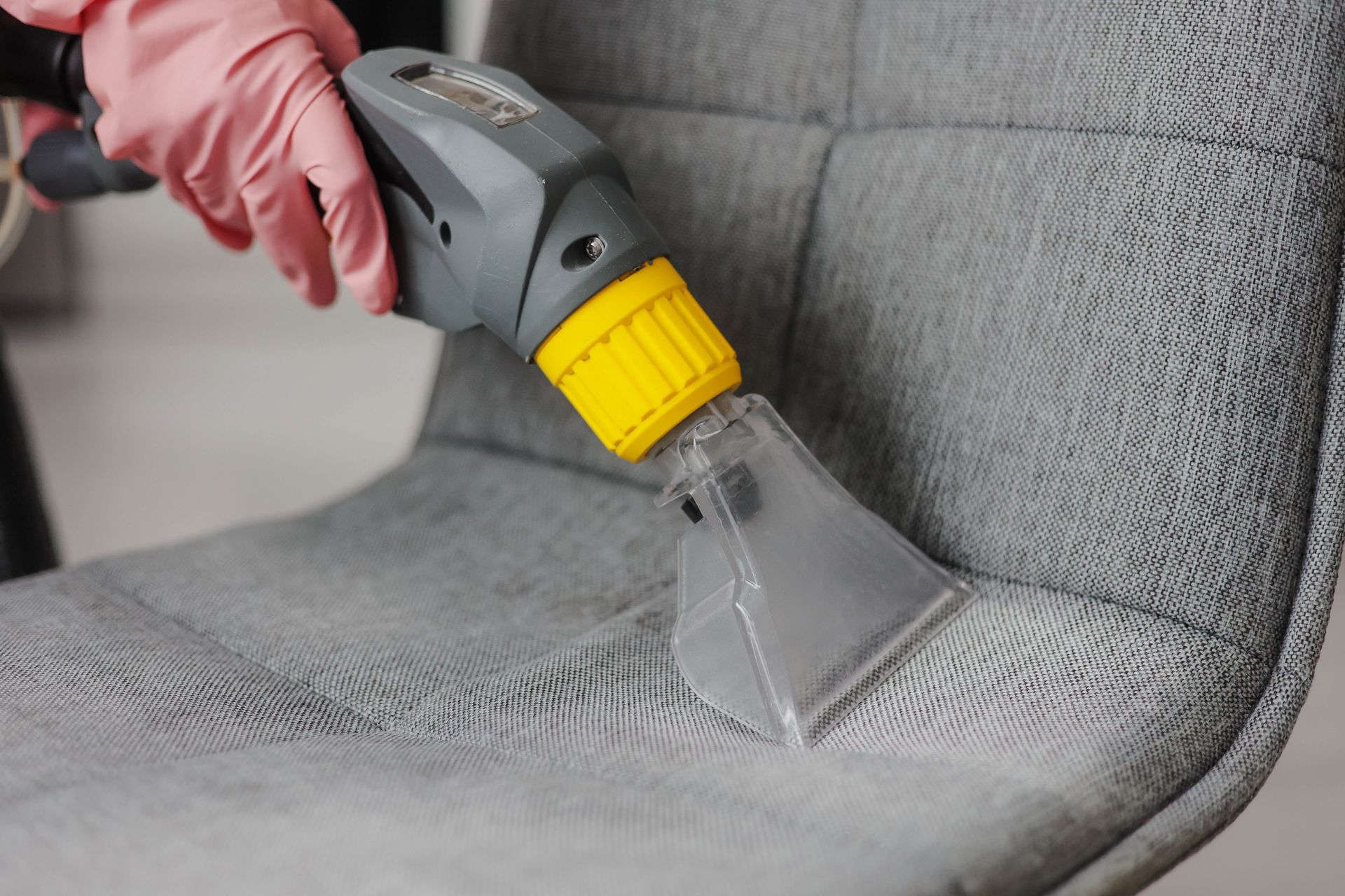 Handheld upholstery cleaner spraying gray fabric chair Handheld upholstery cleaner spraying gray fabric chair