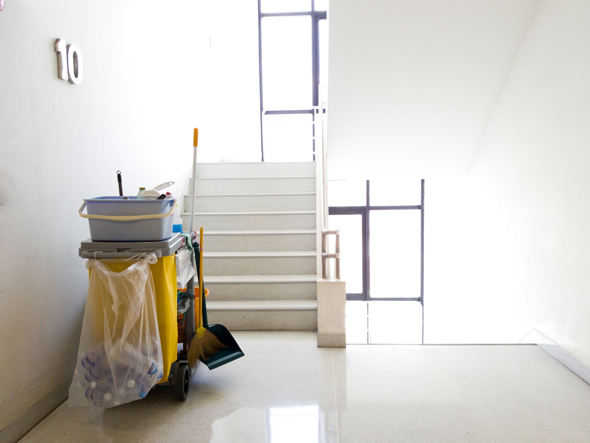 Cleaning cart with supplies beside a staircase in a bright, modern building.