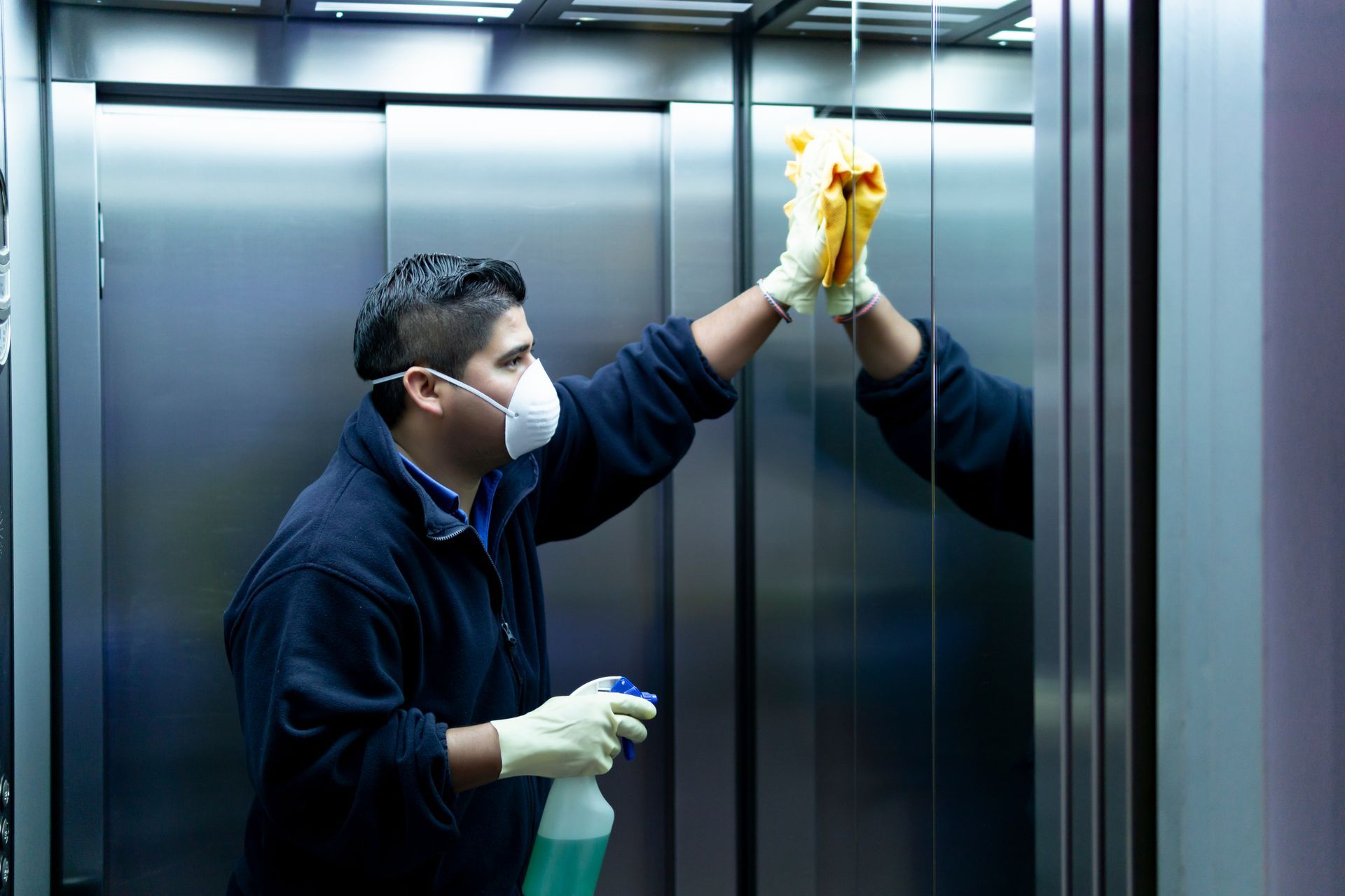 Person in mask and gloves cleaning a mirror in an elevator. Person in mask and gloves cleaning a mirror in an elevator.