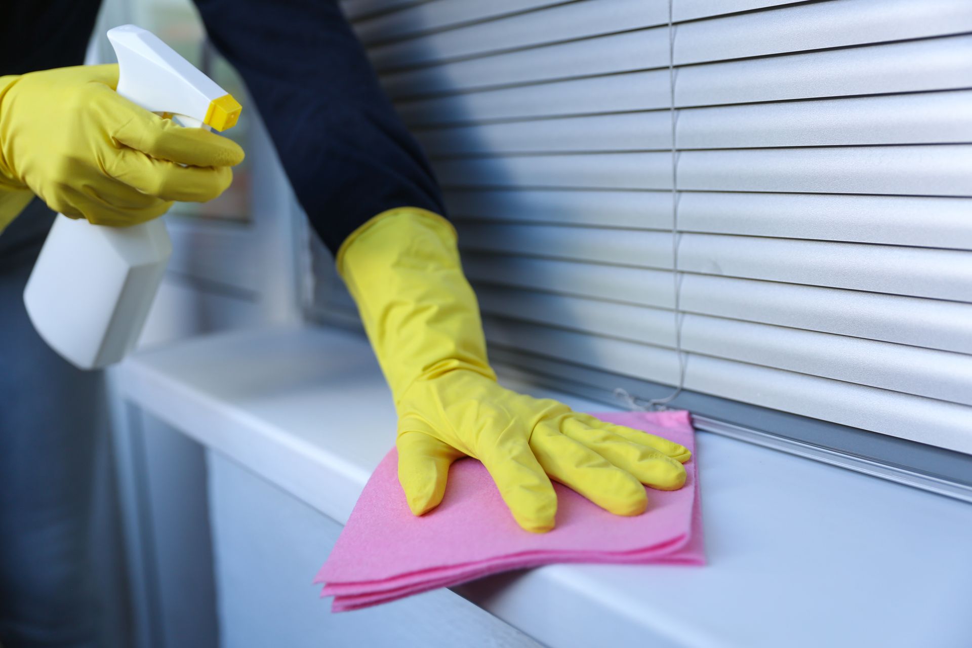 Gloved hands cleaning a window sill with a pink cloth and spray bottle Gloved hands cleaning a window sill with a pink cloth and spray bottle