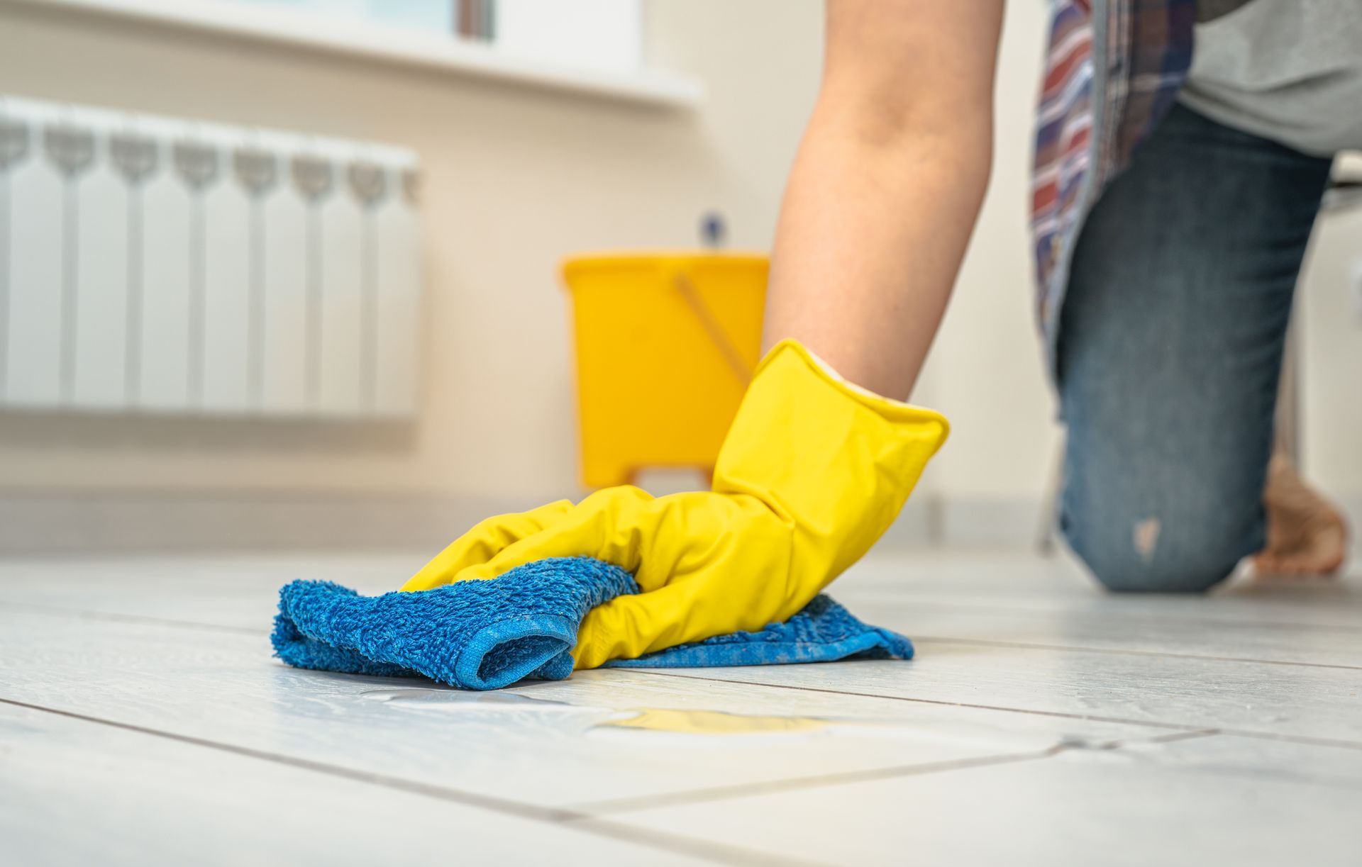 Gloved hands wiping a tiled floor with a blue cloth in a kitchen or utility room Gloved hands wiping a tiled floor with a blue cloth in a kitchen or utility room