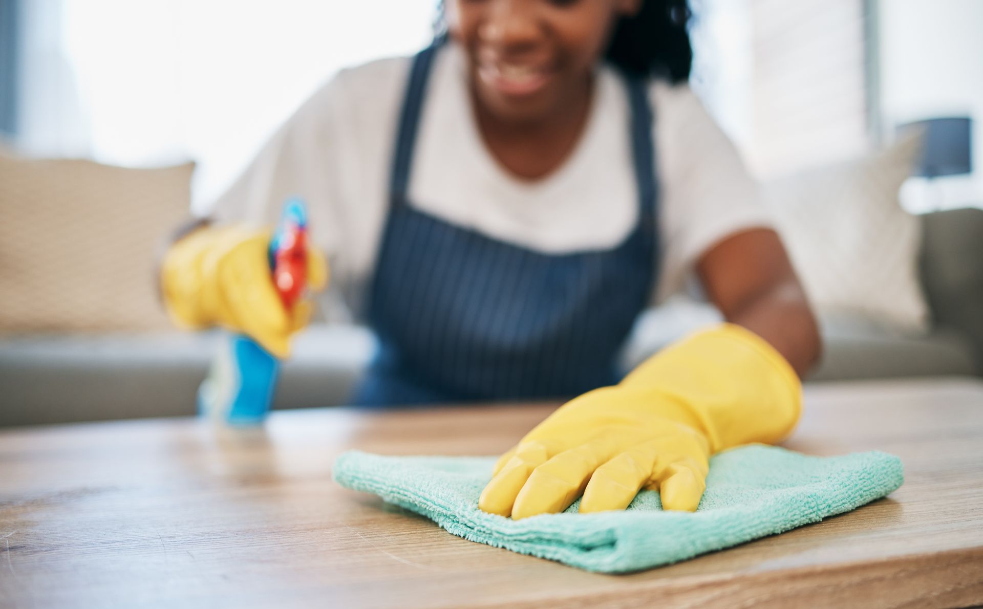 Two people cleaning an office: one mopping, the other wiping a desk, both wearing aprons and gloves.