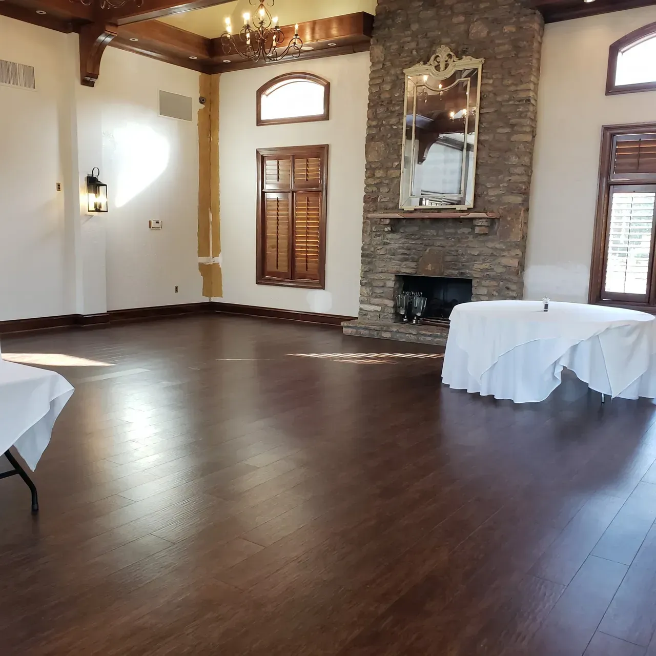 Large room with dark wood floor, fireplace, and two tables covered in white linens. Large room with dark wood floor, fireplace, and two tables covered in white linens.