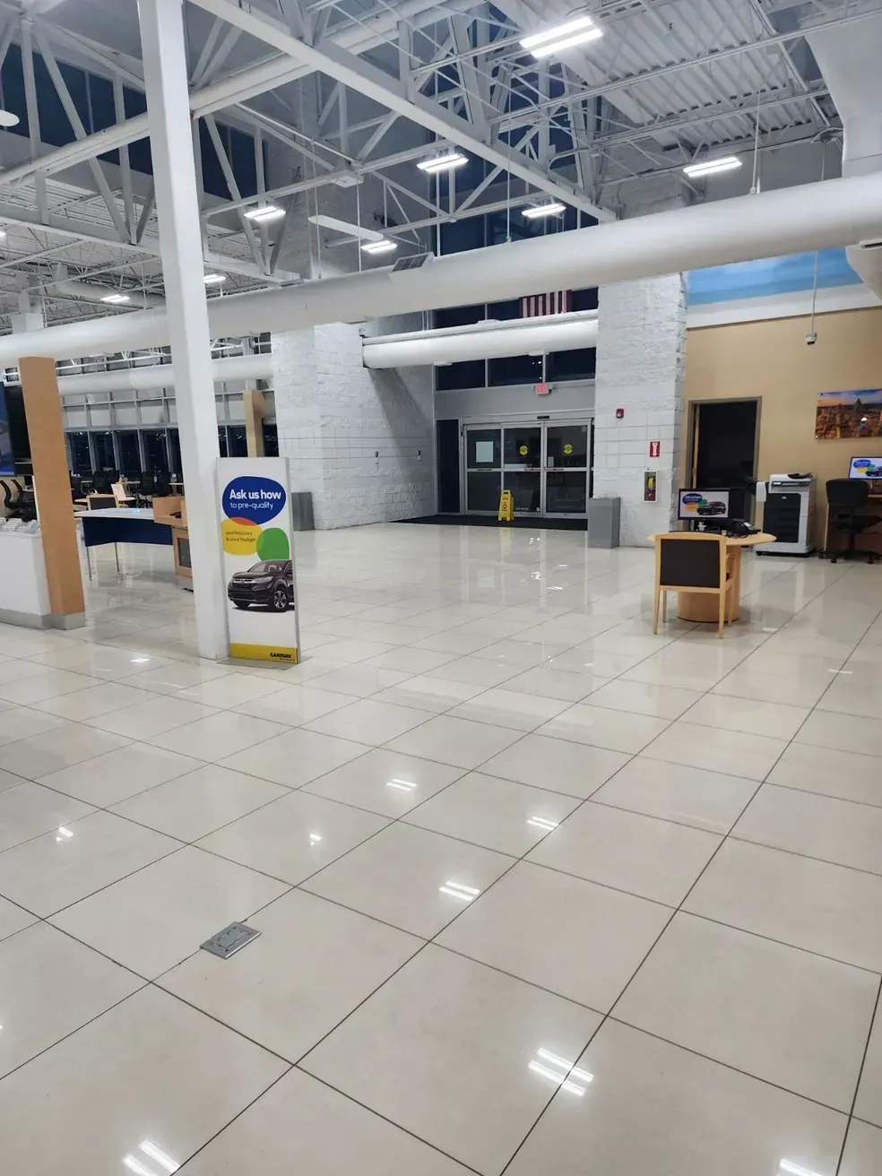 Empty, well-lit interior of a building, likely a car dealership. White tile floors, overhead lights, and entrance doors. Empty, well-lit interior of a building, likely a car dealership. White tile floors, overhead lights, and entrance doors.