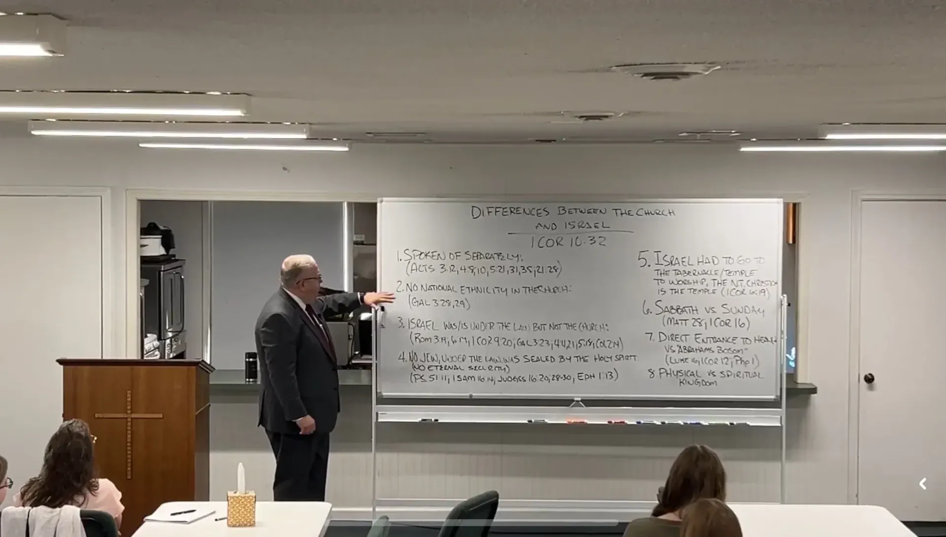 Presenter pointing at a whiteboard covered in writing during a classroom lecture