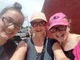 Three smiling friends taking a selfie outdoors, wearing hats and sunglasses.