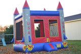 Red, white, and blue USA bounce house with castle turrets on a sidewalk, decorated with stars and stripes.