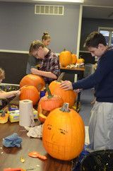 People carving and decorating orange pumpkins on tables in a workshop room