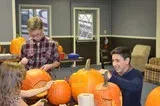 People carving pumpkins at a table in a cozy room with autumn decorations