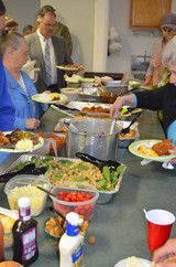 People serving themselves at a buffet table with salads, pasta, and red cups indoors