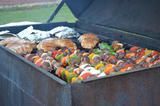 Outdoor grill filled with assorted vegetables, burgers, and fish cooking over charcoal