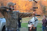 Two archers aiming bows outdoors at sunset, with a third person standing nearby.