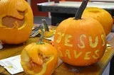 Carved pumpkins with Halloween decorations on a table, including one reading “Jesus Saves.”