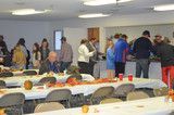 People gathered around tables at an indoor event with food and drinks on white tablecloths.