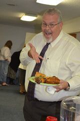 Smiling man in white shirt and tie holding a plate of food at an indoor event