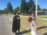 Three people standing and talking on a sunny street near trees and houses