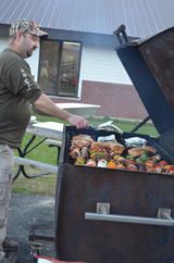 Man grilling colorful vegetables on an outdoor barbecue beside a building