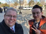 Two people smiling outdoors, one holding up a peace sign in a parking lot.